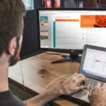 man wearing red earphone sitting on chair while using laptop