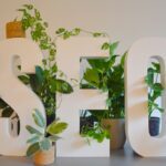 a white sign with plants and a potted plant next to it