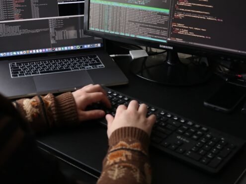 a person sitting at a desk with a laptop and a computer monitor